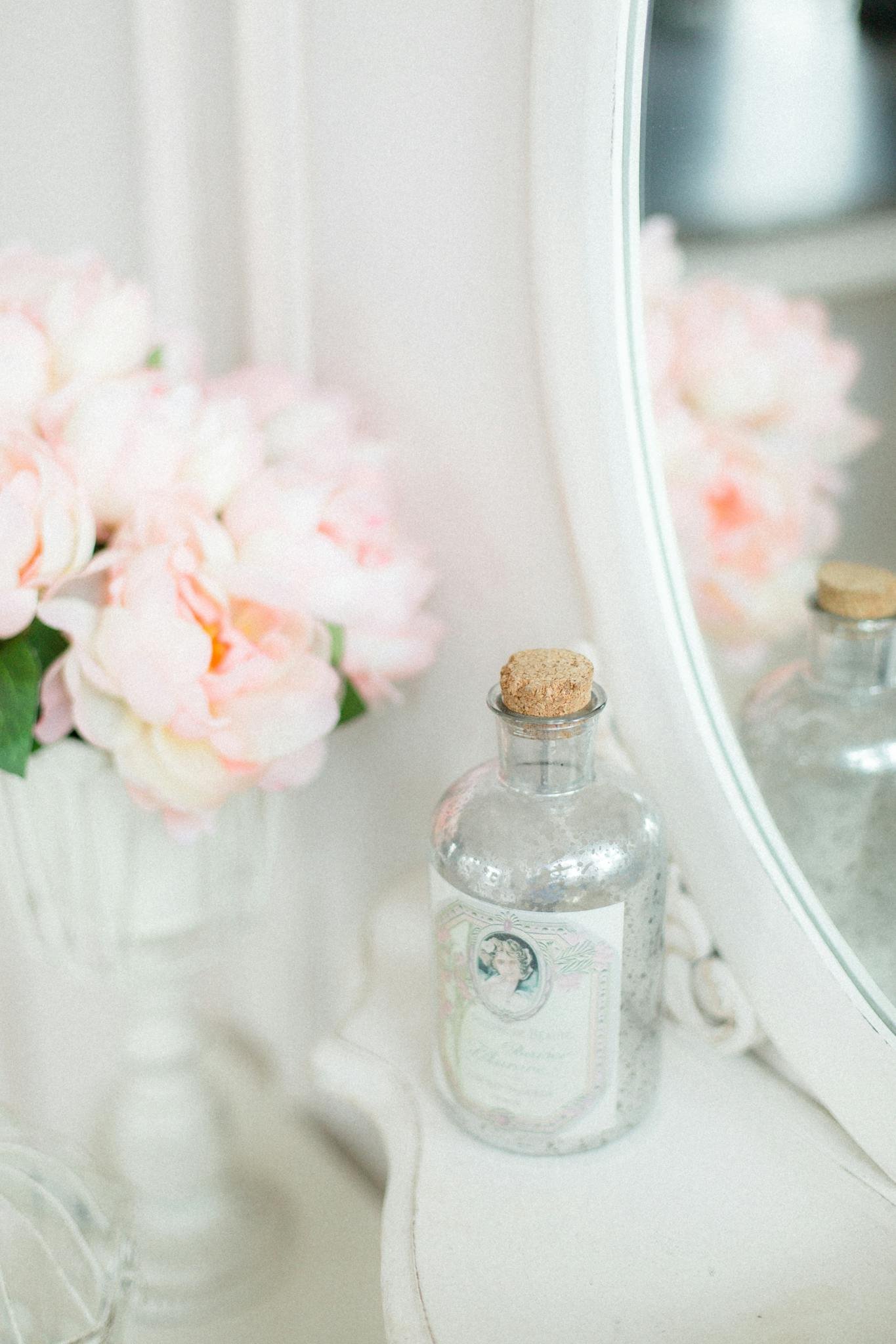 Decorative bottle and vase with aromatic pink flowers placed on white table